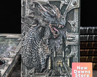 May include: A silver and black journal with a dragon and castle embossed design. The journal has a metal clasp and a textured cover.
