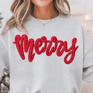 Puede incluir: Sudadera gris claro con la palabra "Merry" en rojo en el pecho. El texto rojo tiene una apariencia texturizada. La sudadera es de estilo casual, adecuada para la temporada navideña.