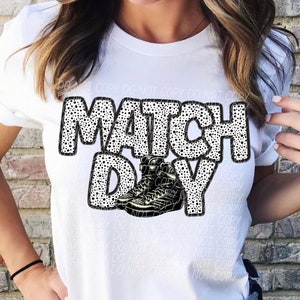 May include: White t-shirt with the text "MATCH DAY" in black letters with white polka dots.  A pair of black and white sneakers are below the text.