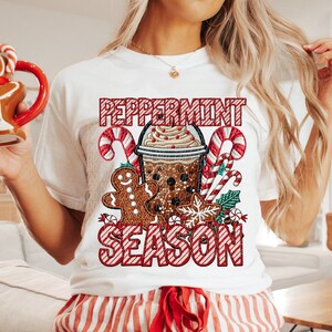 Puede incluir: Camiseta blanca con un gr&aacute;fico festivo de "Peppermint Season". El dise&ntilde;o presenta un moca de menta, un hombre de jengibre, bastones de caramelo y un copo de nieve. El texto est&aacute; en rayas rojas y blancas, perfecto para la temporada navide&ntilde;a.