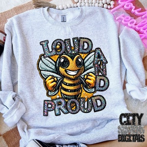 May include: A light gray sweatshirt featuring a cartoon bee with the words "LOUD AND PROUD" in a colorful, jeweled font. The bee is yellow and black with a smiling face and outstretched arms. The sweatshirt has long sleeves.
