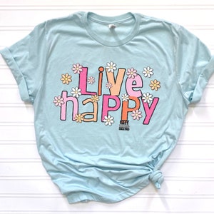 May include: Light blue t-shirt with the text "Live Happy" in colorful letters surrounded by white daisies.