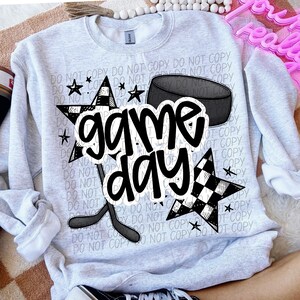 May include: A gray sweatshirt with a black and white checkered star, a hockey stick, a puck, and the text "game day".