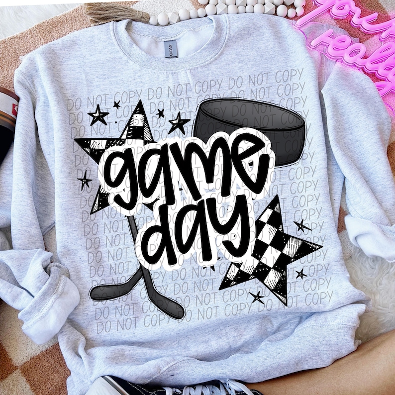 May include: A gray sweatshirt with a black and white checkered star, a hockey stick, a puck, and the text "game day".