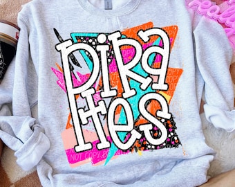 May include: A light grey sweatshirt featuring the word "PIRATES" in a white, distressed font. The word is set against a colourful, abstract design with pink, orange, and teal accents. The sweatshirt has a crew neck and long sleeves.