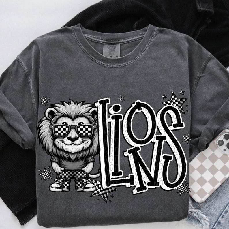 May include: Dark gray sweatshirt featuring a cartoon lion wearing checkered sunglasses and matching shoes. The word "LIONS" is printed in a bold, stylized font with checkered accents. A phone case with a checkered pattern is visible.