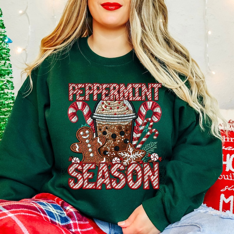 Puede incluir: Sudadera verde oscuro con un gr&aacute;fico festivo. El gr&aacute;fico presenta una bebida navide&ntilde;a, hombre de jengibre, bastones de caramelo y las palabras "Peppermint Season" en rojo y blanco. La sudadera es una prenda de vestir de temporada y acogedora.