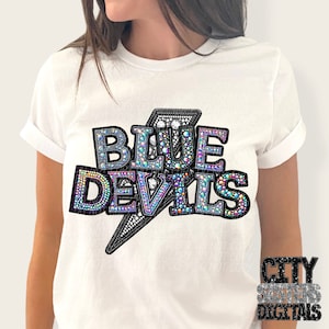 Peut inclure: T-shirt blanc avec un motif d'éclair noir et les mots "BLUE DEVILS" en strass irisés.