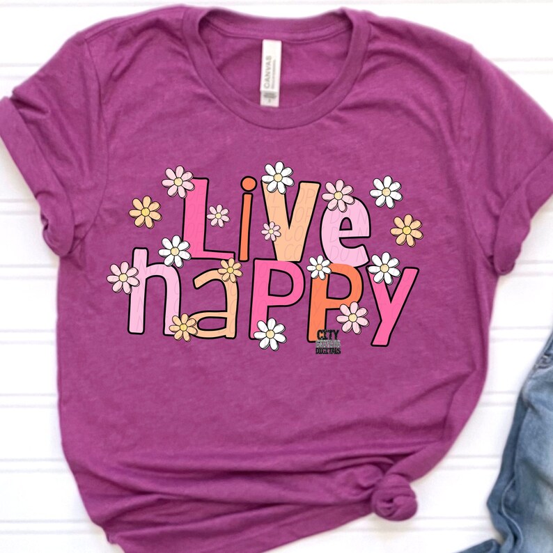 May include: A purple t-shirt with the text "Live happy" in pink, orange, and white letters. The letters are surrounded by white daisies with pink and orange centers.