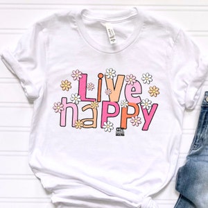 May include: White t-shirt with the text "Live happy" in pink, orange, and white letters surrounded by small white daisies.
