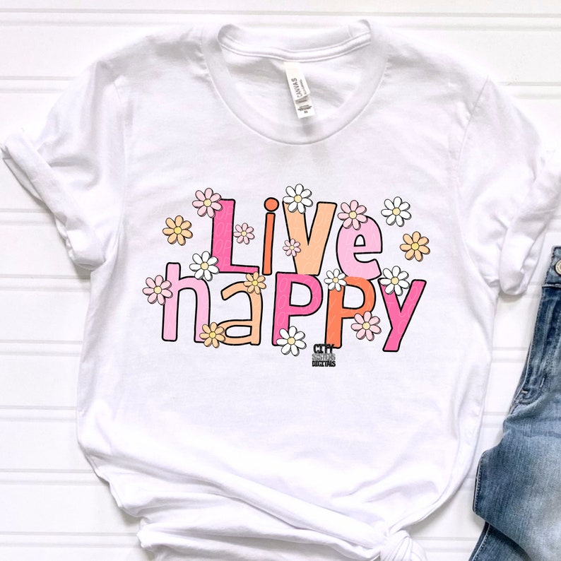 May include: White t-shirt with the text "Live happy" in pink, orange, and white letters surrounded by small white daisies.