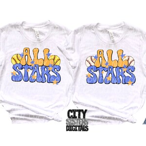 Pu&ograve; includere: Due magliette bianche con il testo "All Stars" in lettere blu e arancioni con stelle gialle e grafica da softball.