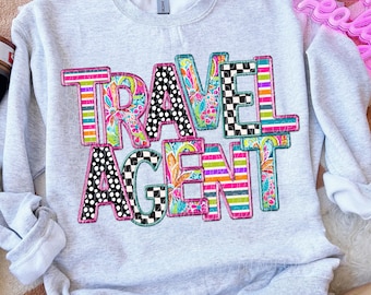 Peut inclure: Un sweat-shirt gris avec les mots "TRAVEL AGENT" en lettres de patchwork colorées. Les lettres sont composées de différents motifs, notamment des pois, des rayures et des motifs floraux.