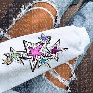 May include: A light blue sweatshirt with a design of colorful stars on the front. The stars are outlined in black and have a white background.