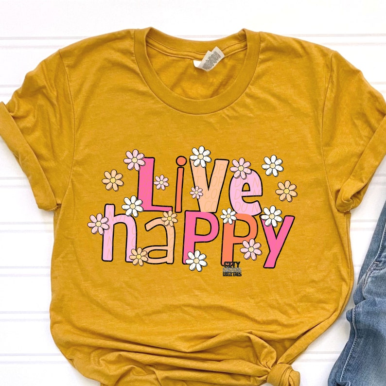 May include: A mustard yellow t-shirt with the text "Live Happy" in pink, orange, and white letters surrounded by white daisies. The text is in a retro font style.