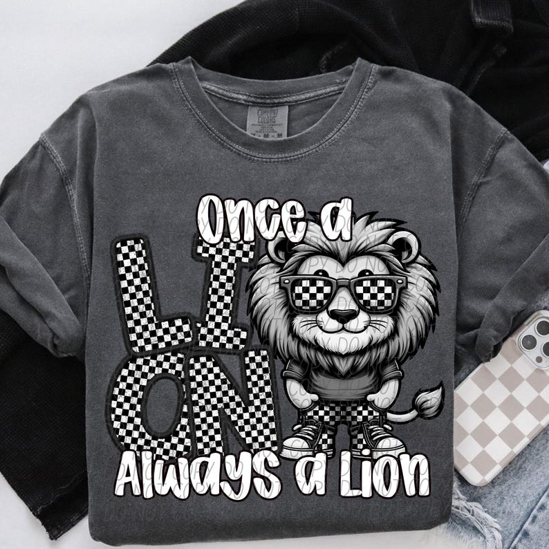 May include: A gray t-shirt with a black and white checkered design and a cartoon lion wearing sunglasses. The text "Once a Lion Always a Lion" is printed on the shirt.