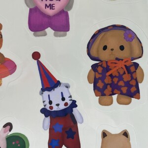 May include: A sheet of stickers featuring various cartoon animal characters. One sticker shows a gray cat holding a pink heart with the words "HUG ME". Other stickers include a bear in a clown outfit, and a bear with a painter's palette.