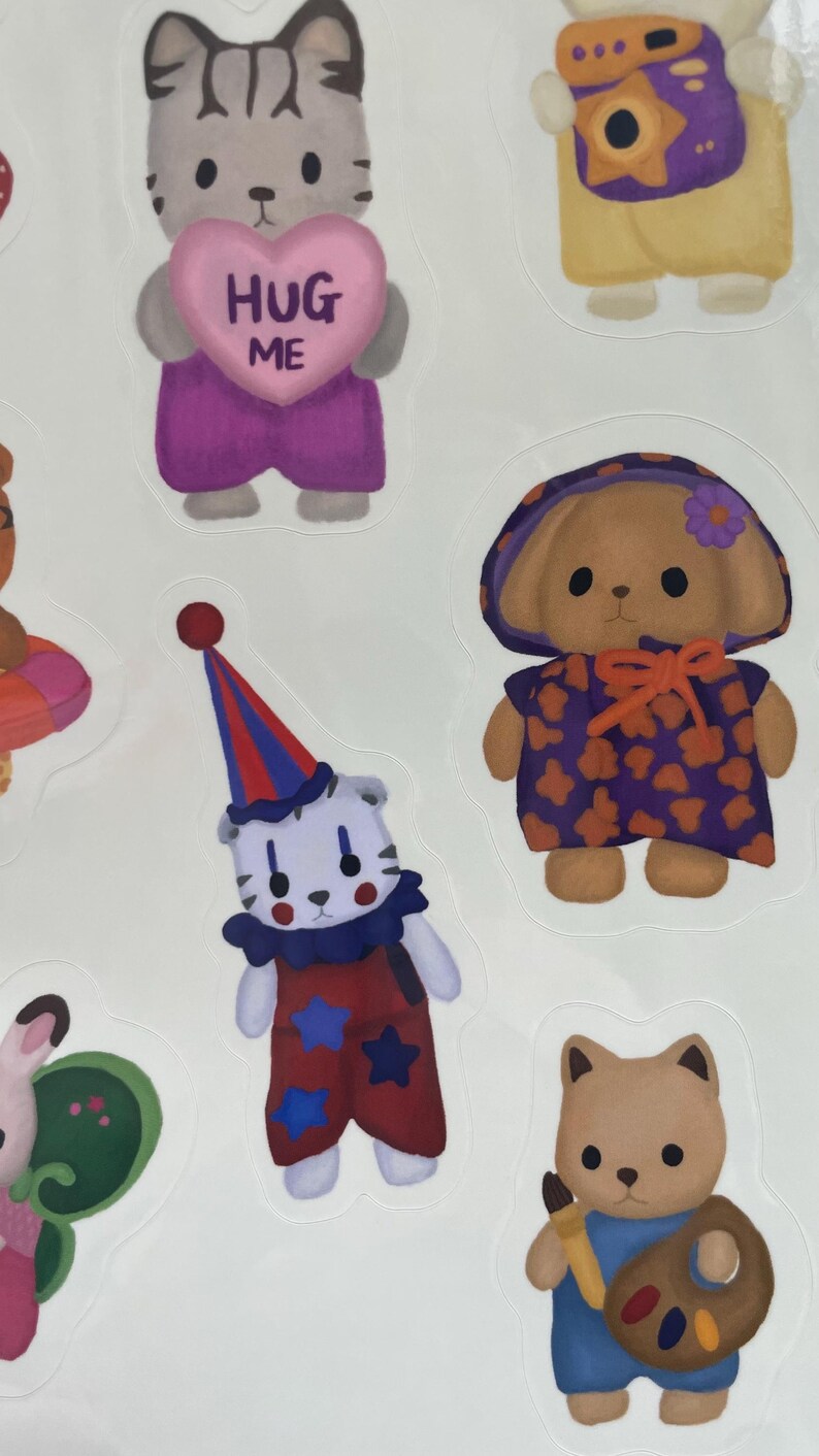 May include: A sheet of stickers featuring various cartoon animal characters. One sticker shows a gray cat holding a pink heart with the words "HUG ME". Other stickers include a bear in a clown outfit, and a bear with a painter's palette.