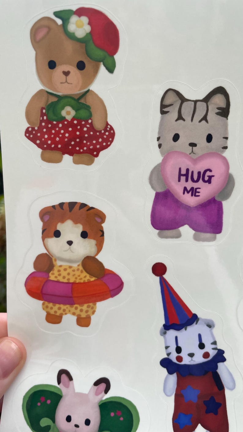 May include: A sheet of colorful stickers featuring cartoon animals. The stickers include a bear in a red dress, a cat holding a pink heart with "HUG ME" on it, a tiger with a swim ring, a clown, and a bunny.