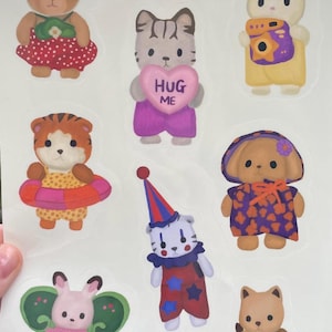 May include: A sheet of colorful stickers featuring various animal characters. The stickers include a bear, cat holding a heart that says "HUG ME", bunny with a camera, tiger with a float, clown, dog, and a bunny with butterfly wings.
