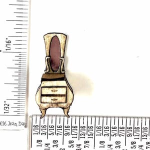 May include: A miniature wooden dresser with a mirror, featuring a light brown finish and two drawers. The mirror has a pinkish hue. The dresser is approximately 1 inch (2.54 cm) tall. The design is reminiscent of antique furniture.