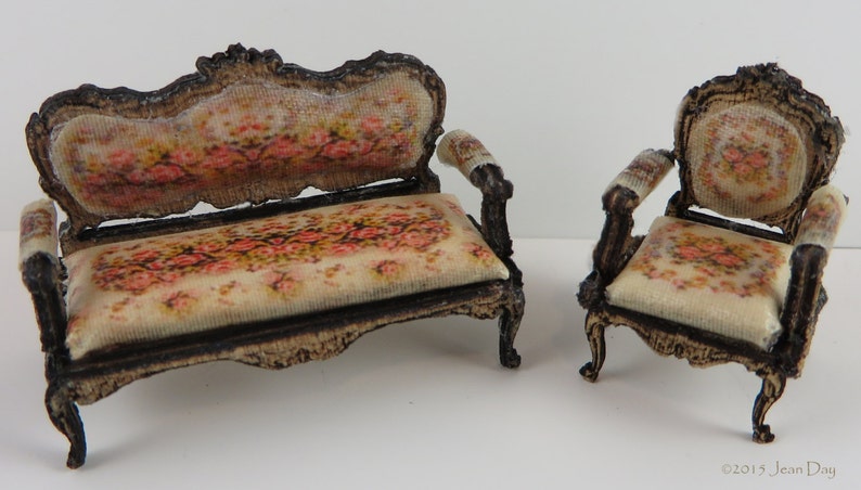 May include: A miniature set of a floral patterned couch and armchair with ornate wooden frames.