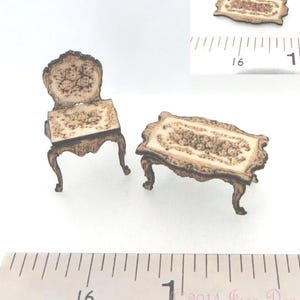 Puede incluir: Un conjunto de silla y mesa rectangular en miniatura con una superficie de color crema con estampado floral y bordes de color marrón oscuro. Se ve una regla que indica que la mesa mide unos 3,8 cm de largo.