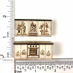 Puede incluir: Dos elementos de cocina en miniatura de madera con detalles grabados con láser. La pieza superior muestra tres casas encantadas, mientras que la inferior representa una estufa con cuatro quemadores y cuatro calabazas en las puertas del armario.