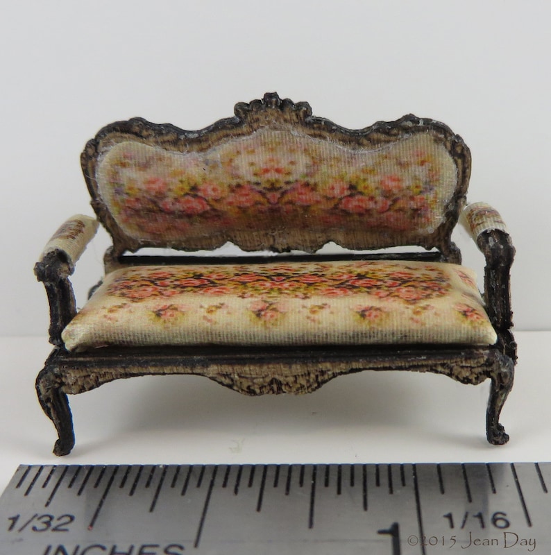 May include: A miniature, ornate, wooden sofa with a floral patterned fabric upholstery. The sofa is approximately 1/16th of an inch in size.