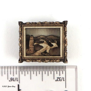 Może przedstawiać: Obraz w drewnianej ramie z rzeźbioną sceną dwóch ptaków przelatujących nad latarnią morską. Obraz ma około 3,5 cm szerokości.