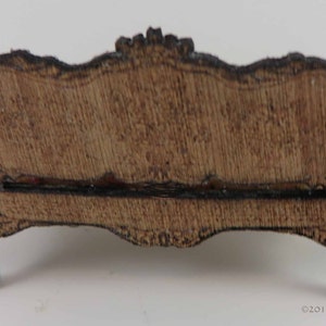 May include: A wooden miniature sofa with a carved design and a brown finish. The sofa has a curved back and scrolled legs.