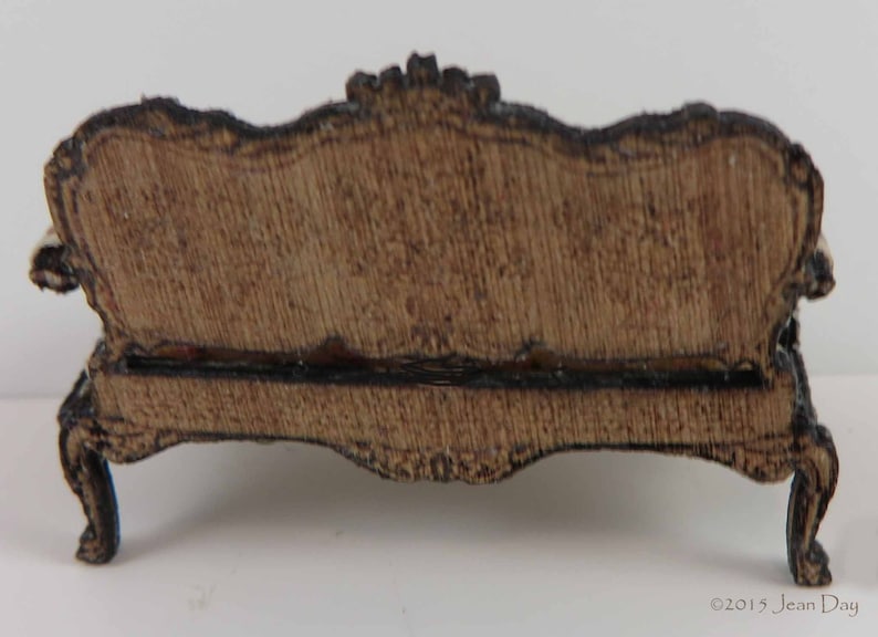 May include: A wooden miniature sofa with a carved design and a brown finish. The sofa has a curved back and scrolled legs.