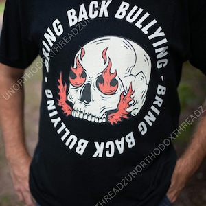 May include: Black t-shirt with a white skull graphic encircled by the words "BRING BACK BULLYING." The skull has flames for eyes and around the jawline. The shirt is a crew neck and appears to be made of cotton.