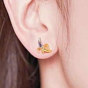May include: A pair of gold banana earrings. The earrings are small and delicate, and they feature a realistic banana design.