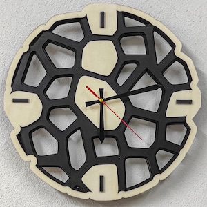 Könnte beinhalten: Eine schwarze und weiße Wanduhr aus Holz mit geometrischem Design. Die Uhr hat schwarze Zeiger und einen roten Sekundenzeiger.