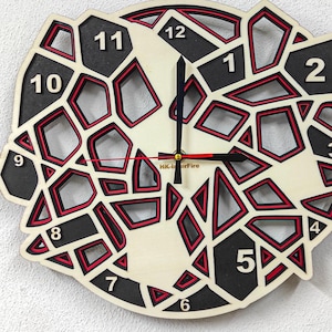 Könnte beinhalten: Eine weiße Holzuhr mit schwarzen und roten geometrischen Formen und schwarzen Zahlen. Das Zifferblatt der Uhr ist von einem schwarzen Rahmen umgeben. Die Zeiger der Uhr sind schwarz und rot.