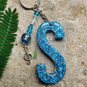 Llavero azul con la letra S, cuentas de vidrio y clave de sol, hecho a mano con cuentas de resina.