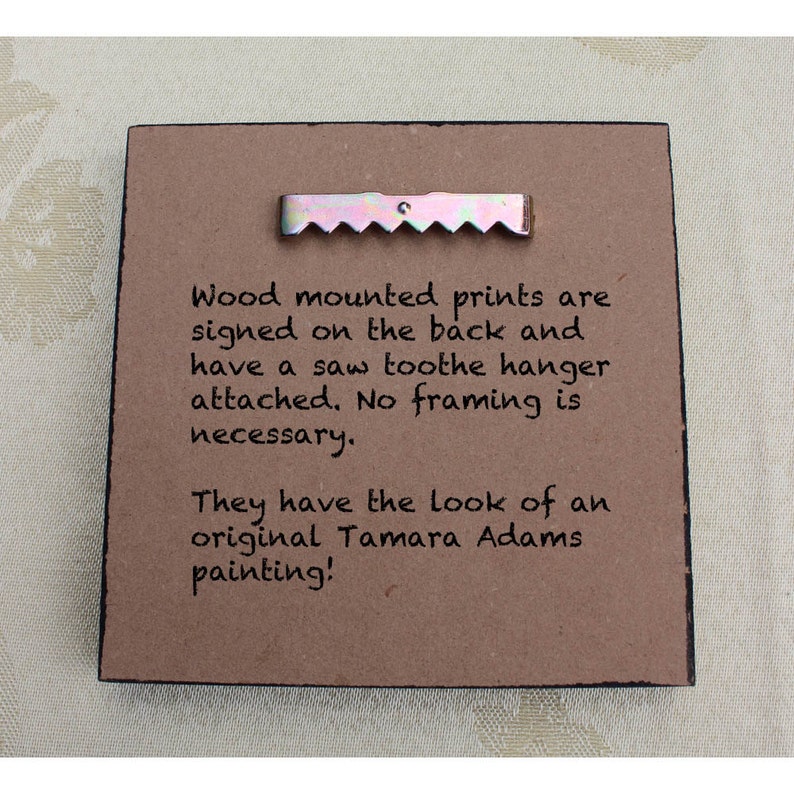 May include: A close-up of a brown wood-mounted print with a sawtooth hanger attached. The print has text that reads: "Wood mounted prints are signed on the back and have a saw toothe hanger attached. No framing is necessary. They have the look of an original Tamara Adams painting!"