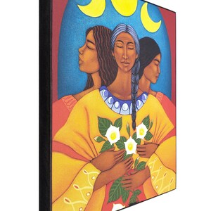 May include: Three women with dark hair and brown skin are depicted in a painting. They are wearing yellow robes and holding white flowers. The background is a blue sky with three yellow crescent moons.