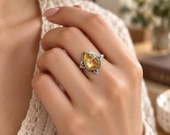 May include: A sterling silver ring featuring a faceted, pear-shaped yellow citrine gemstone. The metal setting displays intricate oxidized detailing around the stone, with small silver beads accentuating the points of the teardrop-shaped frame.