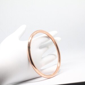 May include: A simple, polished, rose gold bangle bracelet.