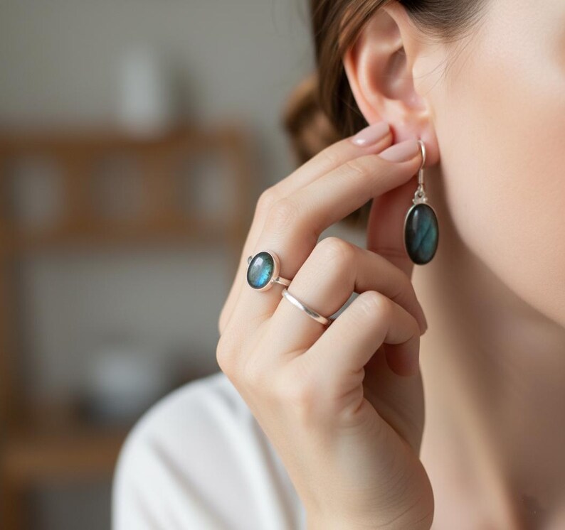 May include: A silver ring featuring an oval labradorite gemstone with blue iridescence, paired with a simple silver band and a matching silver drop earring containing an oval labradorite stone that displays a similar blue iridescent sheen.