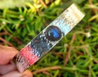 May include: A silver hammered bangle bracelet with a blue labradorite gemstone set in the centre.