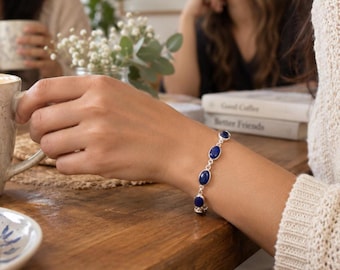 May include: A silver chain bracelet featuring five oval-shaped, deep blue lapis lazuli gemstones set in polished silver bezels. The bracelet is secured with a silver link chain, showcasing a classic design that highlights the vibrant blue stones.