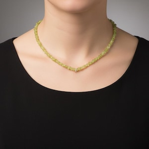 Puede incluir: Un delicado collar con pequeñas piedras preciosas de color verde claro. El collar se lleva sobre una parte superior negra, resaltando el color vibrante de las piedras. El collar parece ser de estilo gargantilla.