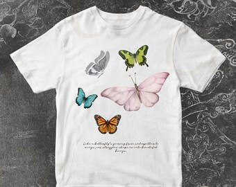 May include: White t-shirt with a graphic of butterflies in various colors and patterns. The text "Like a butterfly's journey from caterpillar to wings, our struggles shape us into beautiful beings." is printed on the bottom of the shirt.