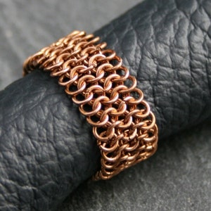 Könnte beinhalten: Ein Kupfer-Kettenhemdring mit einem gewebten Design. Der Ring besteht aus kleinen, miteinander verbundenen Metallringen.