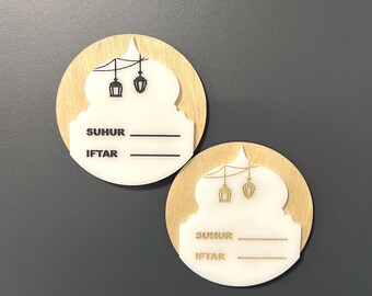 May include: Two round wooden signs with white centers and gold and black accents. The signs feature a mosque silhouette with hanging lanterns and the words "SUHUR" and "IFTAR" with blank lines underneath.