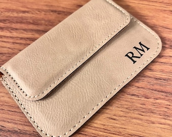 May include: A beige leather card holder with a flap closure and the initials "RM" embossed on the front.
