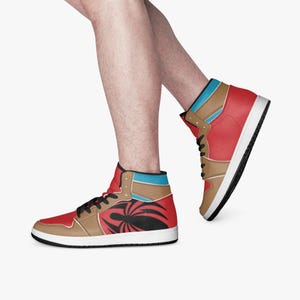 May include: High-top sneakers in red, tan, and blue with a black and white graphic design. The sneakers have black laces and a white sole. The shoes are shown on a person's feet.